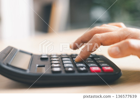 Close-up of a hand pressing calculator keys for budgeting, accounting and financial analysis. Business expense planning, tax calculation, office desk background, copy space for paperwork. Close-up of a hand pressing calculator keys for budgeting, accounting and financial analysis. Business expense planning, tax calculation, office desk background, copy space for paperwork. 136577639