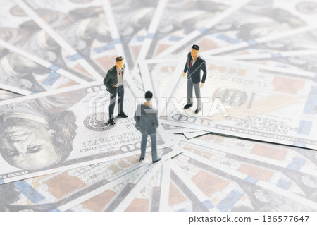 Miniature businessmen meeting on spread US dollar banknotes, symbolizing investment, negotiation and financial strategy. Business finance concept with cash background and copy space. Miniature businessmen meeting on spread US dollar banknotes, symbolizing investment, negotiation and financial strategy. Business finance concept with cash background and copy space. 136577647