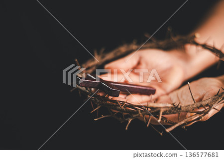 Hand placing a wooden cross above a crown of thorns on an open Bible, dark background and dramatic light with copy space, symbolizing crucifixion, sacrifice, Holy Week and Easter faith. Hand placing a wooden cross above a crown of thorns on an open Bible, dark background and dramatic light with copy space, symbolizing crucifixion, sacrifice, Holy Week and Easter faith. 136577681