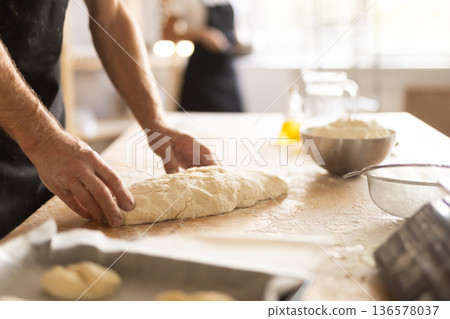 Baker's hands rolling out raw dough in bakery 136578037