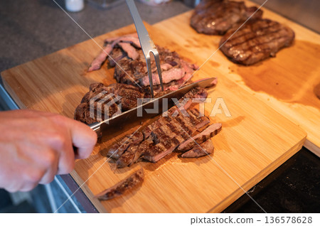 Grilled steak being sliced on wooden cutting board with knife and fork Grilled steak being sliced on wooden cutting board with knife and fork 136578628