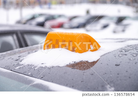 Snow-covered taxi roof sign in winter parking lot scene Snow-covered taxi roof sign in winter parking lot scene 136578654