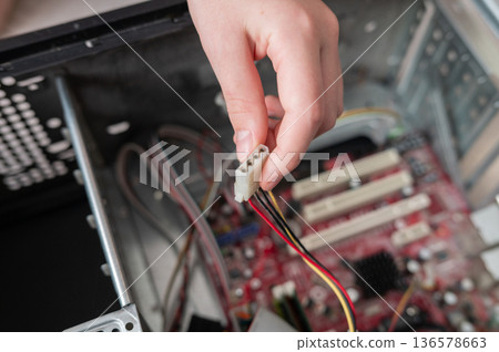 Young caucasian hand connecting power cable to computer motherboard interior Young caucasian hand connecting power cable to computer motherboard interior 136578663