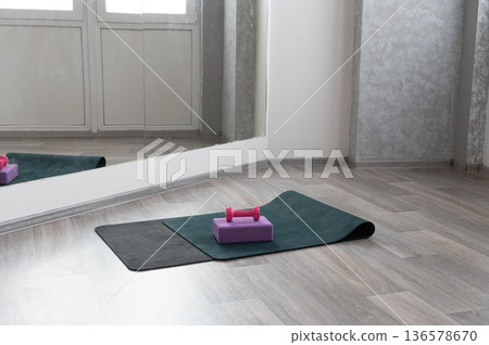Home yoga studio with exercise mat, foam block, and dumbbells on wooden floor 136578670