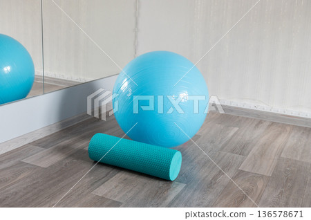 Blue exercise ball and foam roller on wooden floor near a mirror Blue exercise ball and foam roller on wooden floor near a mirror 136578671