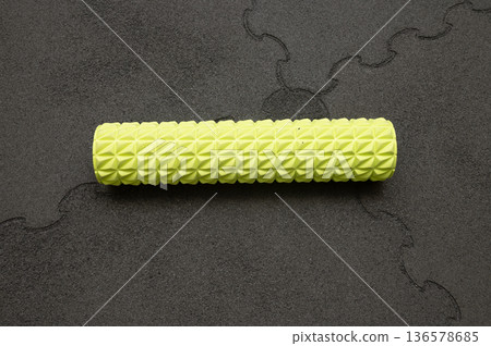 Yellow textured foam roller on gray puzzle mat for fitness and muscle relief 136578685