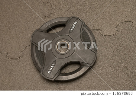 Black 15kg weight plate on puzzle mat for strength training workouts Black 15kg weight plate on puzzle mat for strength training workouts 136578693