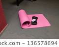 Pink yoga mat, eye mask, and pillow on gray floor in gym setting 136578694
