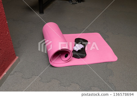 Pink yoga mat, eye mask, and pillow on gray floor in gym setting 136578694