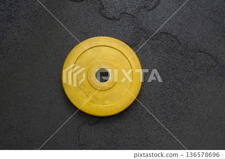 Yellow weight plate on gym floor for strength training and fitness 136578696