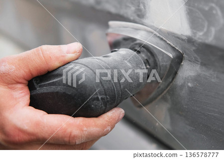 Car body shop. Repair man processes the welding seam using an angle grinder on replaced car part. Professional Body master grind old paint and rust. Rust damage. Rusting car. Hands with tool close-up Car body shop. Repair man processes the welding seam using an angle grinder on replaced car part. Professional Body master grind old paint and rust. Rust damage. Rusting car. Hands with tool close-up 136578777