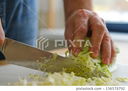 Handsome bearded man is preparing green fresh vegan salad in the kitchen at home. Male cutting vegetables, lettuce with knife on wooden chopping board, cooking vegetarian meal. Tasty healthy diet food 136578792