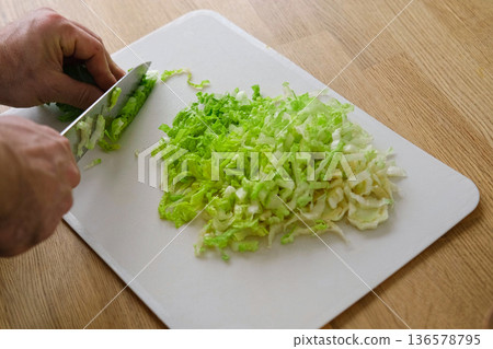 Handsome bearded man is preparing green fresh vegan salad in the kitchen at home. Male cutting vegetables, lettuce with knife on wooden chopping board, cooking vegetarian meal. Tasty healthy diet food Handsome bearded man is preparing green fresh vegan salad in the kitchen at home. Male cutting vegetables, lettuce with knife on wooden chopping board, cooking vegetarian meal. Tasty healthy diet food 136578795