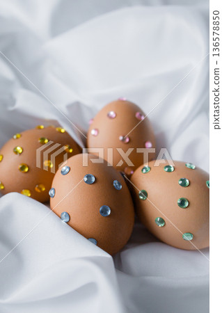Easter eggs decorated with colorful crystal rhinestones on white silky fabric close up 136578850
