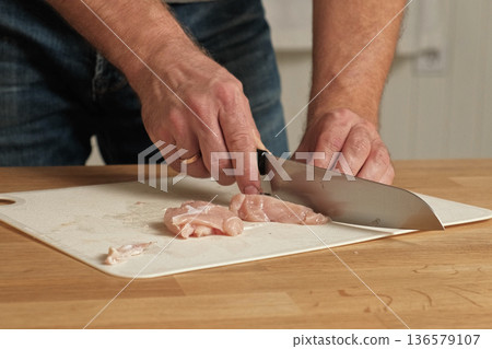 Man butcher cut raw meat with sharp knife at home kitchen. Male person cutting the chicken fillet pieces for cooking. Preparing chopping food. Split poultry breast. Healthy lean meat, low cholesterol Man butcher cut raw meat with sharp knife at home kitchen. Male person cutting the chicken fillet pieces for cooking. Preparing chopping food. Split poultry breast. Healthy lean meat, low cholesterol 136579107