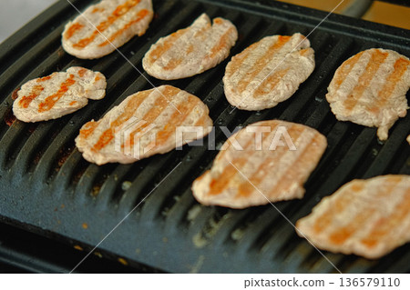 Modern Electric grill. Close-up of beef steak, chop cooking on barbecue metal grill at home kitchen. Portable compact grill roasting food. Burger patties grilling process. Cook turn around minced meat 136579110