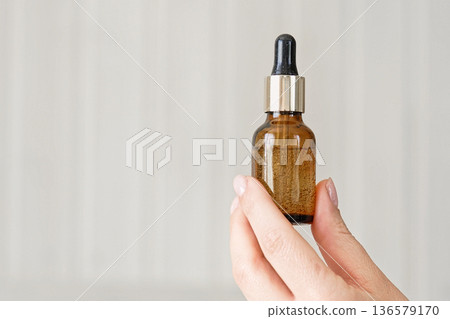 Female hands showing natural oil cosmetics on a Beige Background. Dropper amber brown glass Bottle with pipette. Spa Beauty products Isolate on Neutral Backdrop. Skincare recommend, makeup advertising Female hands showing natural oil cosmetics on a Beige Background. Dropper amber brown glass Bottle with pipette. Spa Beauty products Isolate on Neutral Backdrop. Skincare recommend, makeup advertising 136579170