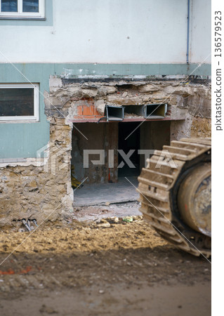 Heavy machinery dismantling damaged facade of residential building during renovation works, construction site with debris and exposed structure. Heavy machinery dismantling damaged facade of residential building during renovation works, construction site with debris and exposed structure. 136579523