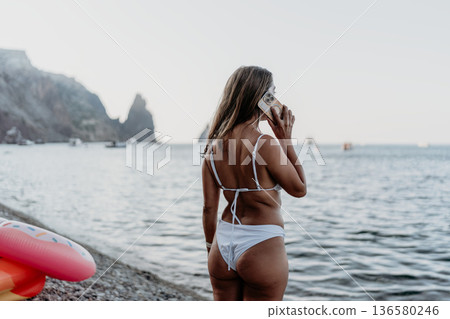 Woman beach phone. Adult female on summer vacation talking on smartphone by ocean shore with copy space. Woman beach phone. Adult female on summer vacation talking on smartphone by ocean shore with copy space. 136580246