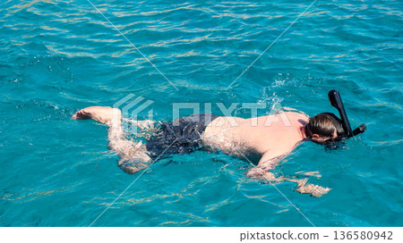 A man in a mask floats on the surface of the Red Sea and looks into the depths A man in a mask floats on the surface of the Red Sea and looks into the depths 136580942