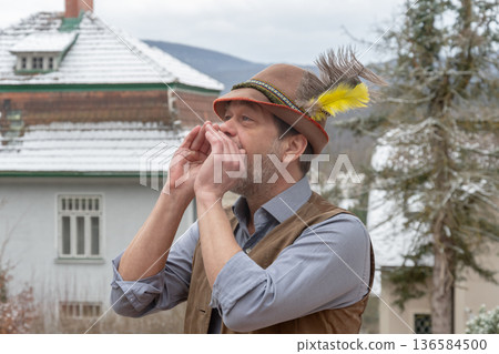 Adult man in Tyrolean hat calling someone outdoors in cold cloudy weather Adult man in Tyrolean hat calling someone outdoors in cold cloudy weather 136584500