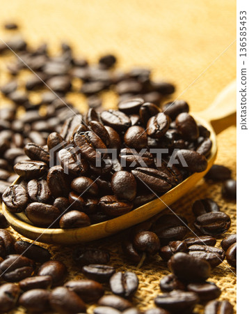 Roasted coffee beans scooped into a wooden measuring spoon Roasted coffee beans scooped into a wooden measuring spoon 136585453