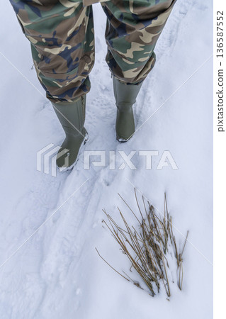 Person walking in snow wearing camouflage pants and boots 136587552
