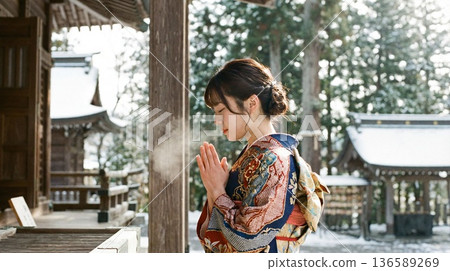 一位身著和服的美麗女子在白雪皚皚的古老神社裡，於清冷的空氣中祈禱。 136589269
