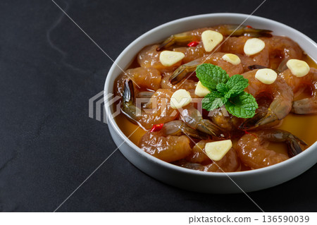 Korean style soy marinated shrimp served with garlic slices, chili, and fresh herbs in a white bowl on dark background. Popular Korean seafood dish known as saeu jang, premium raw shrimp, Korean style soy marinated shrimp served with garlic slices, chili, and fresh herbs in a white bowl on dark background. Popular Korean seafood dish known as saeu jang, premium raw shrimp, 136590039