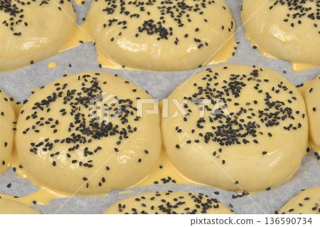 Raw burger buns with black sesame seeds on baking paper 136590734