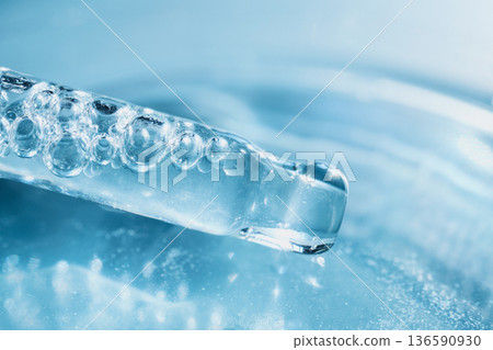 Pipette drawing clear cosmetic serum with bubbles against blue background, symbolizing hydration Pipette drawing clear cosmetic serum with bubbles against blue background, symbolizing hydration 136590930