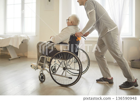 Doctor Or Nurse Moving Elderly Patient In Wheelchair At Nursing Home Or Hospital Doctor Or Nurse Moving Elderly Patient In Wheelchair At Nursing Home Or Hospital 136590948