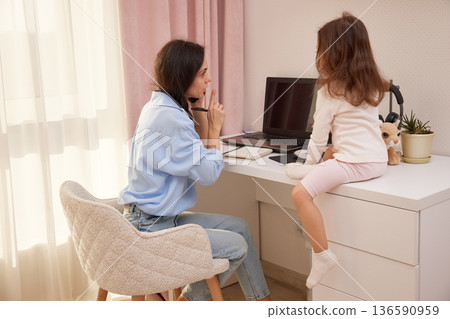 Woman and child sharing a desk, focusing on laptop and notebook during remote work 136590959