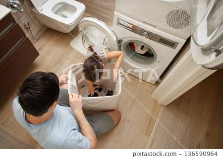 Father and daughter sorting clothes from a laundry basket for washing 136590964