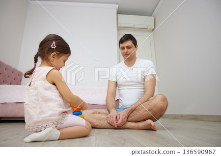 Father and daughter playing with colorful stacking toys on the wooden floor at home 136590967