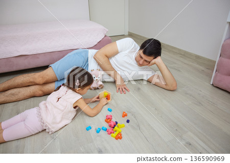 Father and daughter enjoying quality time together, playing with colorful building blocks on floor 136590969