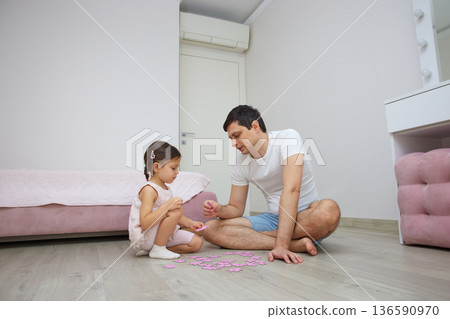 Father and daughter enjoying time together, building a puzzle on the wooden floor 136590970