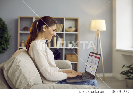 Smiling woman freelancer working on laptop at home, managing budgeting and savings Smiling woman freelancer working on laptop at home, managing budgeting and savings 136591222
