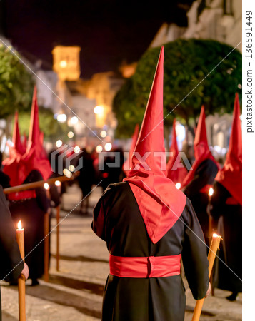 Many nazarenos with red hoods walking in procession 136591449