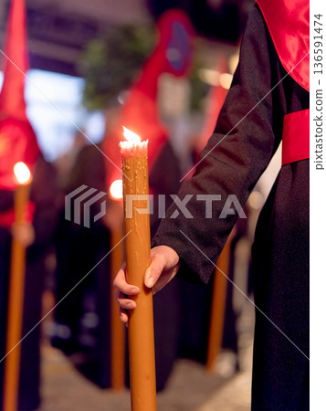 Detailed view of a hand holding a large lit candle in a religious procession 136591474