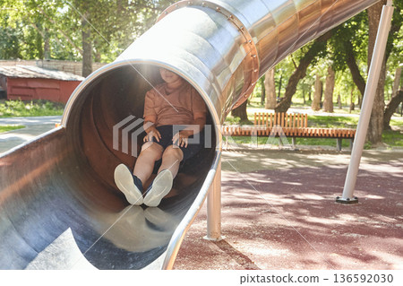 Young caucasian male sliding through playground tube on a sunny day in park Young caucasian male sliding through playground tube on a sunny day in park 136592030