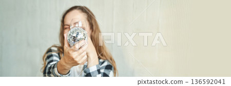 Smiling caucasian young woman holding shiny disco ball in casual plaid shirt Smiling caucasian young woman holding shiny disco ball in casual plaid shirt 136592041
