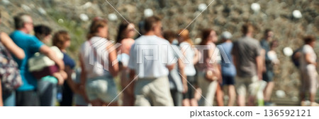 Diverse group of people waiting outdoors in a blurred setting on a sunny day Diverse group of people waiting outdoors in a blurred setting on a sunny day 136592121