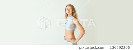 Caucasian young female in athletic attire standing confidently against a white Caucasian young female in athletic attire standing confidently against a white 136592206