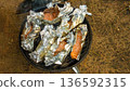 Grilled salmon fillets wrapped in aluminum foil cooking on a charcoal grill in an outdoor setting surrounded by grass and dirt 136592315