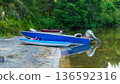 Colorful kayaks and motorboat docked on sandy shore beside calm water surrounded by lush greenery in a serene outdoor setting 136592316