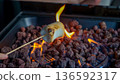 Marshmallow roasting on a skewer over an open flame with glowing embers and rocks in a modern indoor setting 136592317