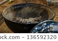 Charcoal grill with ashes and charcoal remnants, surrounded by natural outdoor setting with pine needles and rocks in the background 136592320