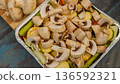 Freshly sliced mushrooms on a bed of colorful vegetables in a foil tray, prepared for cooking in a kitchen setting 136592321