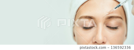 Caucasian female receiving cosmetic injection in forehead for anti-aging 136592336